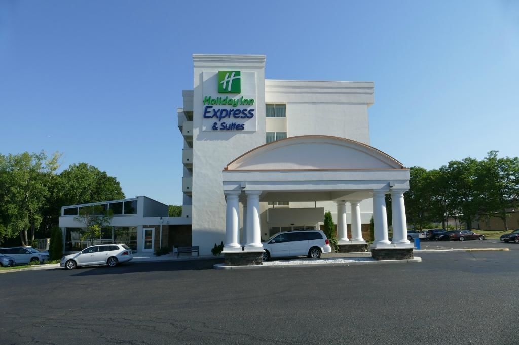 Ein Holiday Inn Express & Suites Hotel mit weißer Fassade, einem überdachten Eingang mit Säulen und einem Parkplatz mit mehreren Autos.