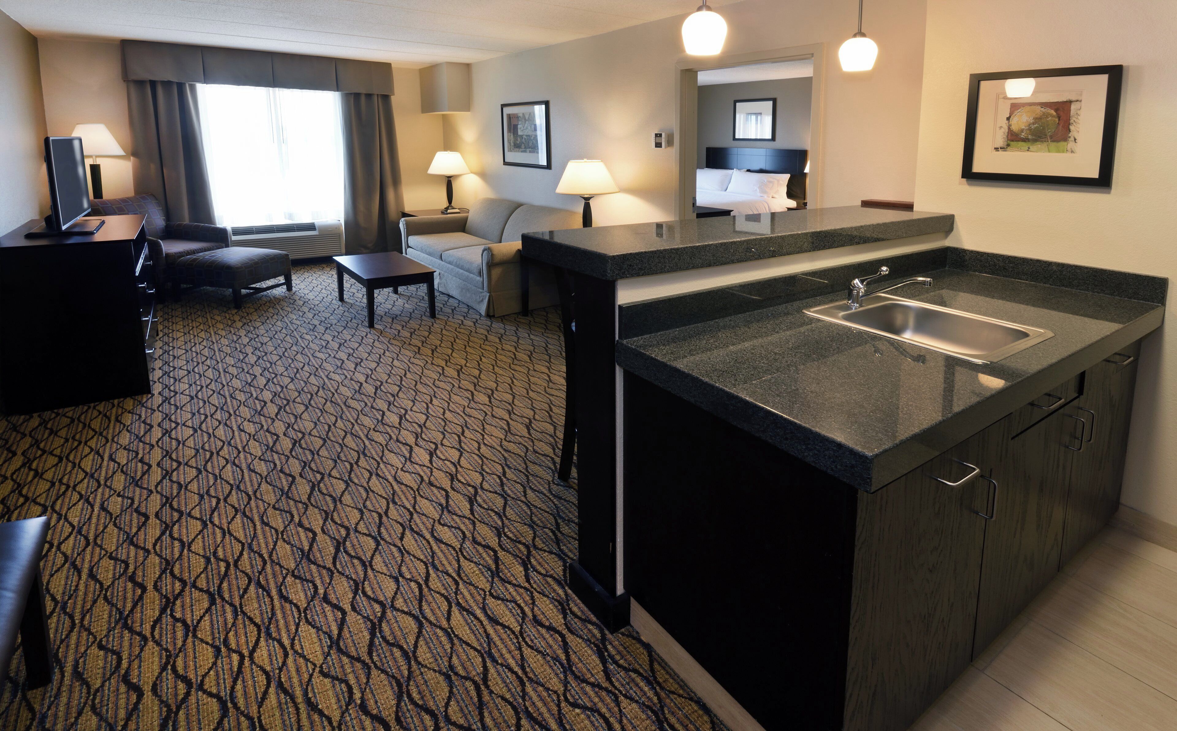 A hotel room with a kitchenette, a sofa, a desk, and a bed.