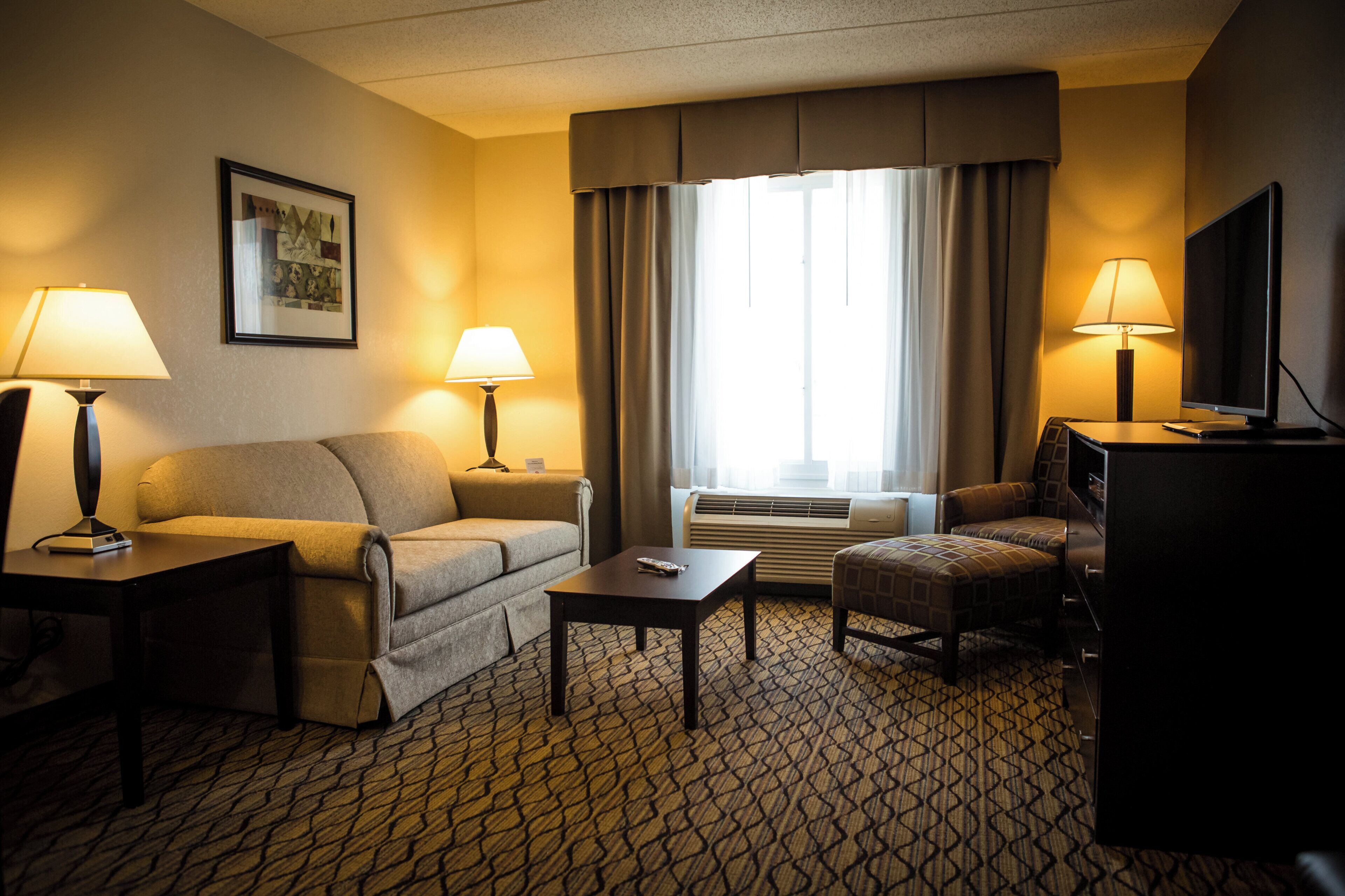 Habitación de hotel con sofá, mesa de centro, televisor y escritorio con lámparas.
