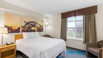 A hotel room with a large bed, a nightstand with a lamp, a chair, and a window with curtains.