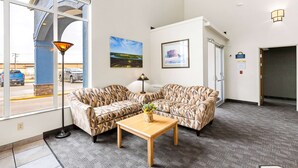 A lobby with patterned sofas, a wooden table with a vase, a lamp, and framed pictures on the wall.