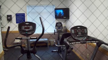 A fitness center with treadmills and elliptical machines, a television screen, and a sign with fitness center rules.