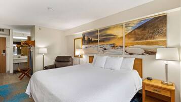 A hotel room with a large bed, a wooden nightstand, a desk with a chair, and a painting of a snowy landscape on the wall.