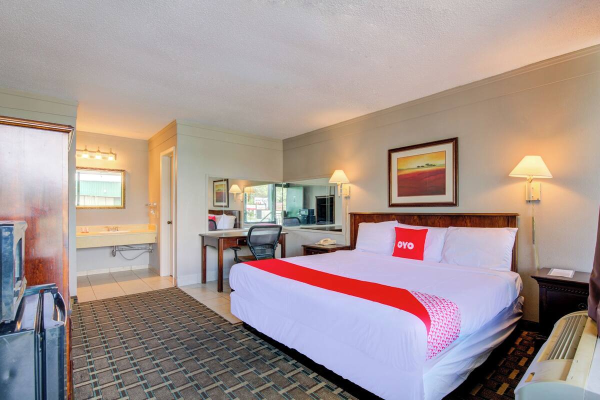 A hotel room with a large bed, a desk, a chair, a bathroom, and a window.