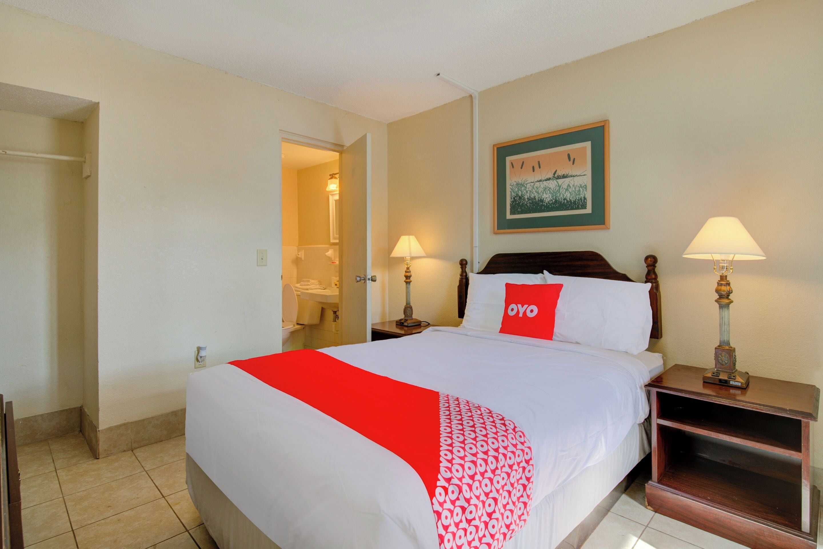Une chambre d’hôtel avec un grand lit, deux tables de chevet avec des lampes, un tableau encadré au mur et une porte de salle de bain entrouverte.