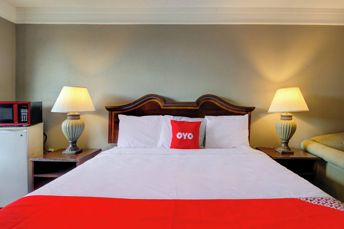 A neatly made bed with white and red bedding, two bedside lamps, a microwave, and a small table.