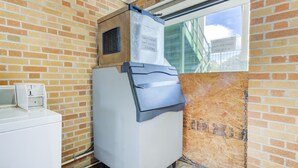 A compact room with a brick wall, a window, a built-in washer and dryer, and a door with a sign indicating guest laundry room availability. -  Hotel Douglas GA US-441 (Douglas)