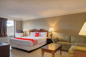 A hotel room with a bed, two bedside tables, a sofa, a coffee table, and a window with curtains. - Rise Inn by OYO US 441 (Douglas)