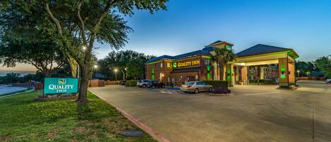 A Quality Inn with a parking lot, a gas station, and a large tree.