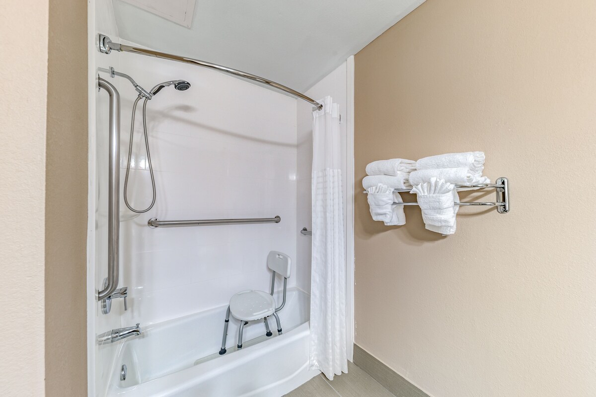 A bathroom with a walk-in shower, grab bars, a small chair, and a towel rack.