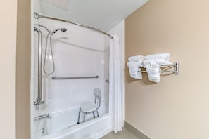 A bathroom with a walk-in shower, grab bars, a small chair, and a towel rack. - Quality Inn West Plano - Dallas (Plano)