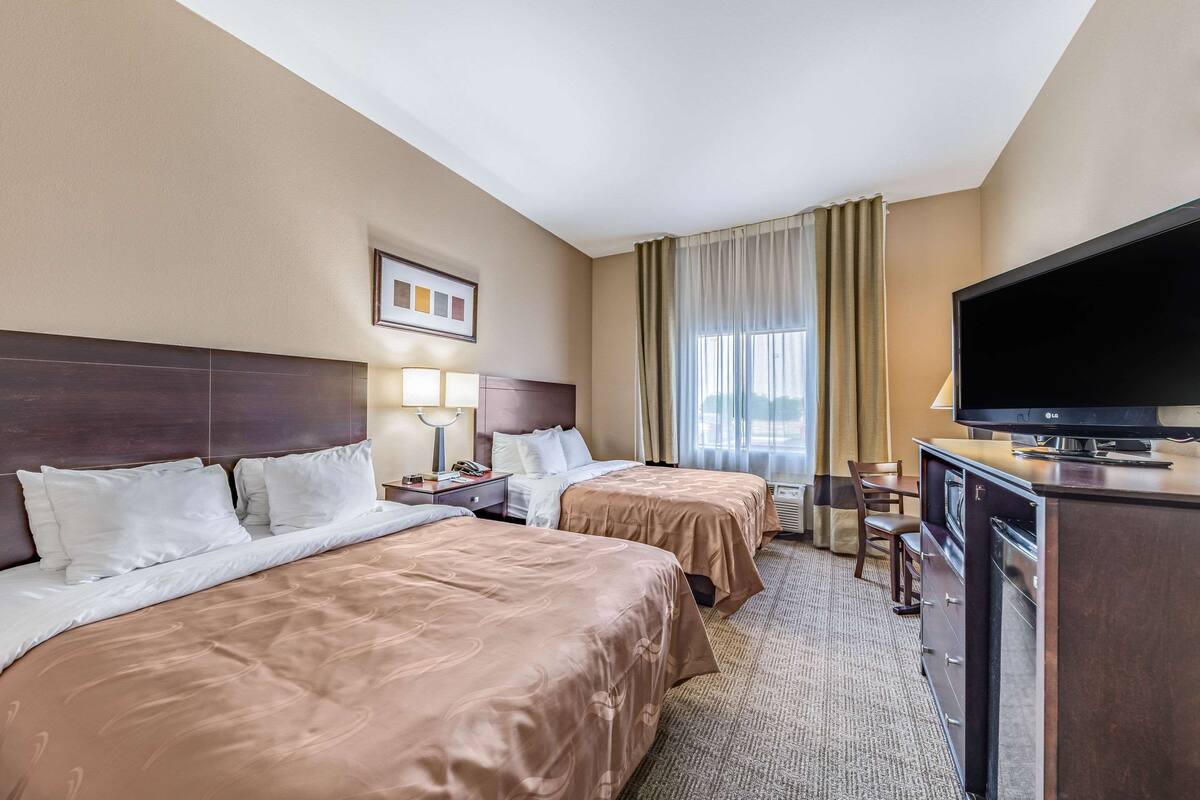 A hotel room with two beds, a TV, a desk, and a chair.