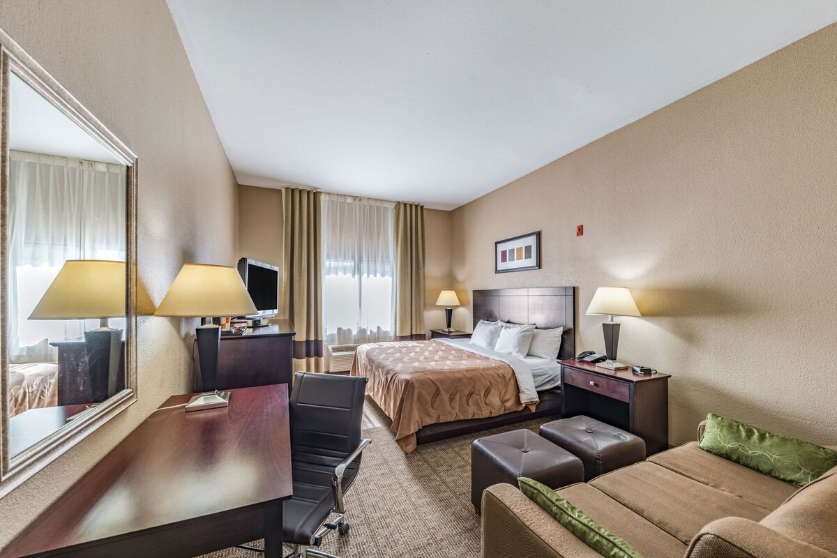 A hotel room with a bed, a desk, a chair, a sofa, and a large mirror.