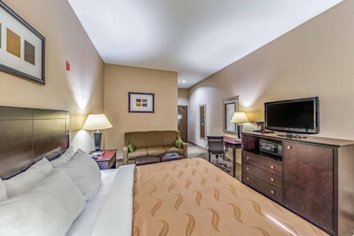 A hotel room with a bed, a sofa, a TV, a desk, and a cabinet.