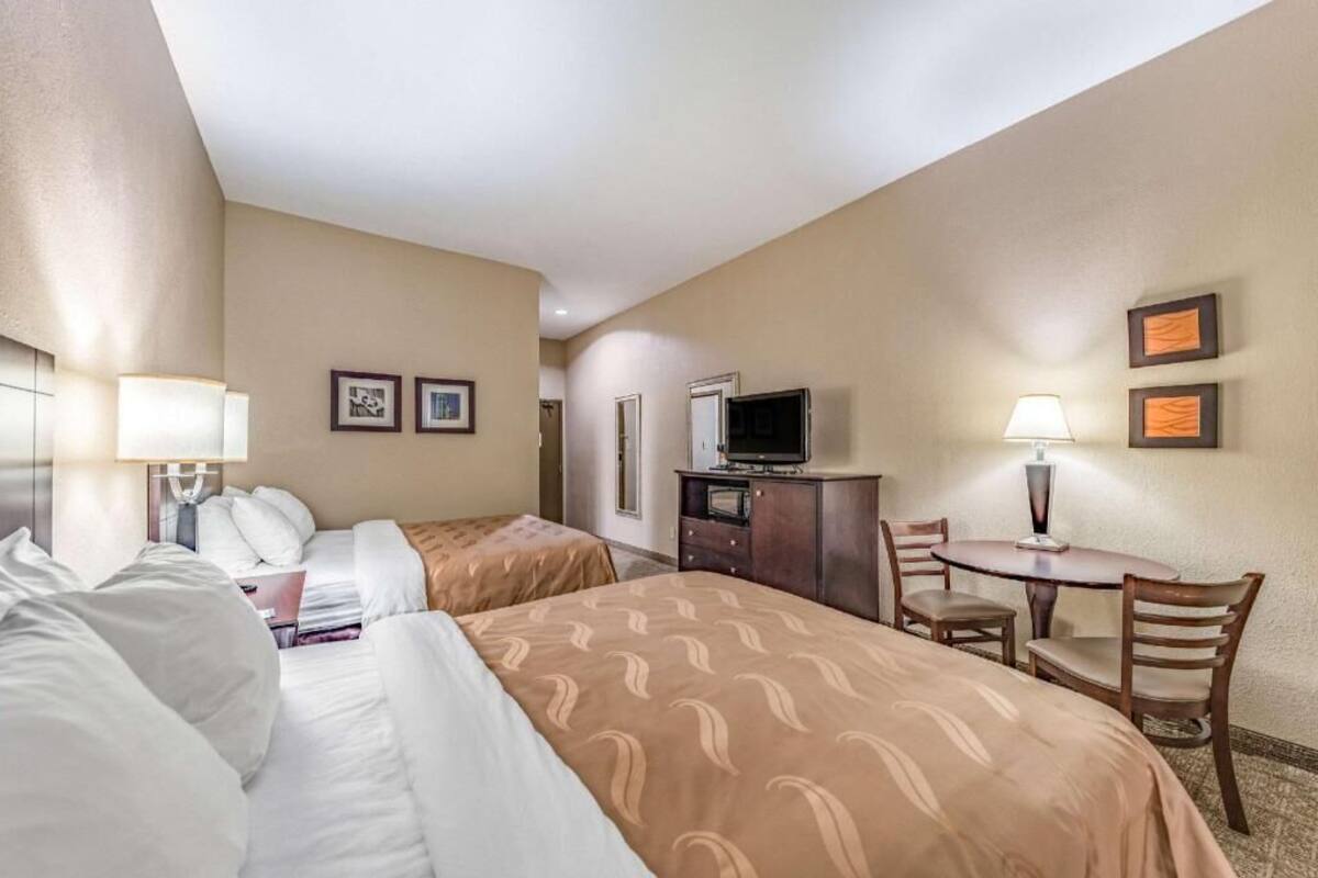 A hotel room with two beds, a desk, a chair, a television, and a small table with a lamp.