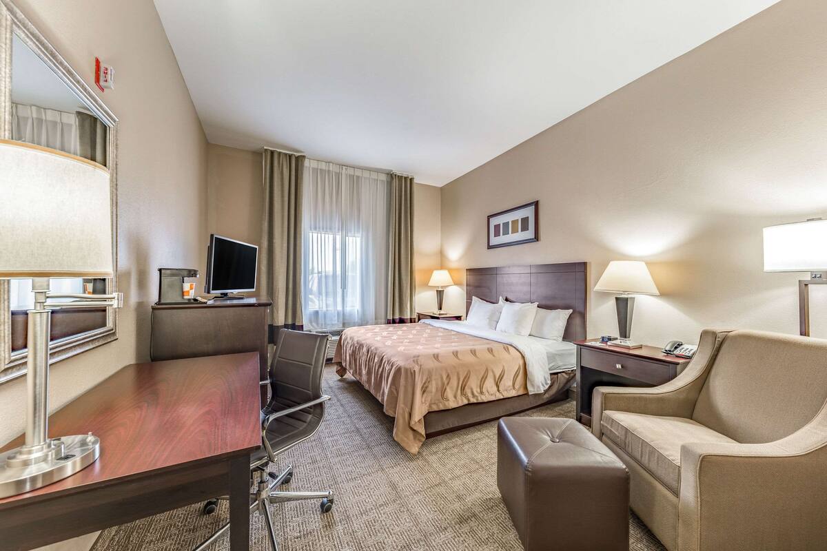 A hotel room with a bed, a desk, a chair, a TV, a lamp, and a bedside table.