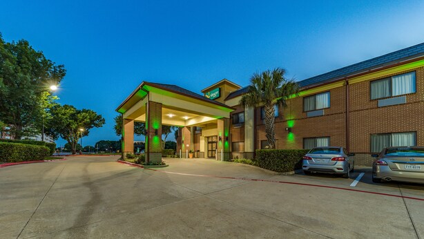 A hotel entrance with a covered parking area, brick exterior, and two cars parked in the lot. - Quality Inn West Plano - Dallas (Plano)