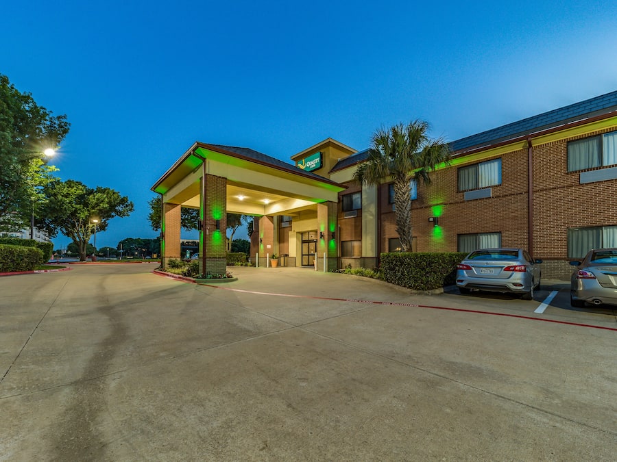 A hotel entrance with a covered parking area, brick exterior, and two cars parked in the lot.