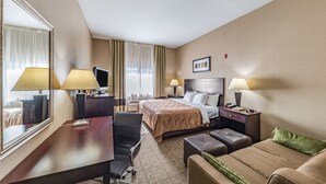 A hotel room with a bed, two bedside lamps, a desk with a chair, a television, and a large mirror. - Quality Inn West Plano - Dallas (Plano)