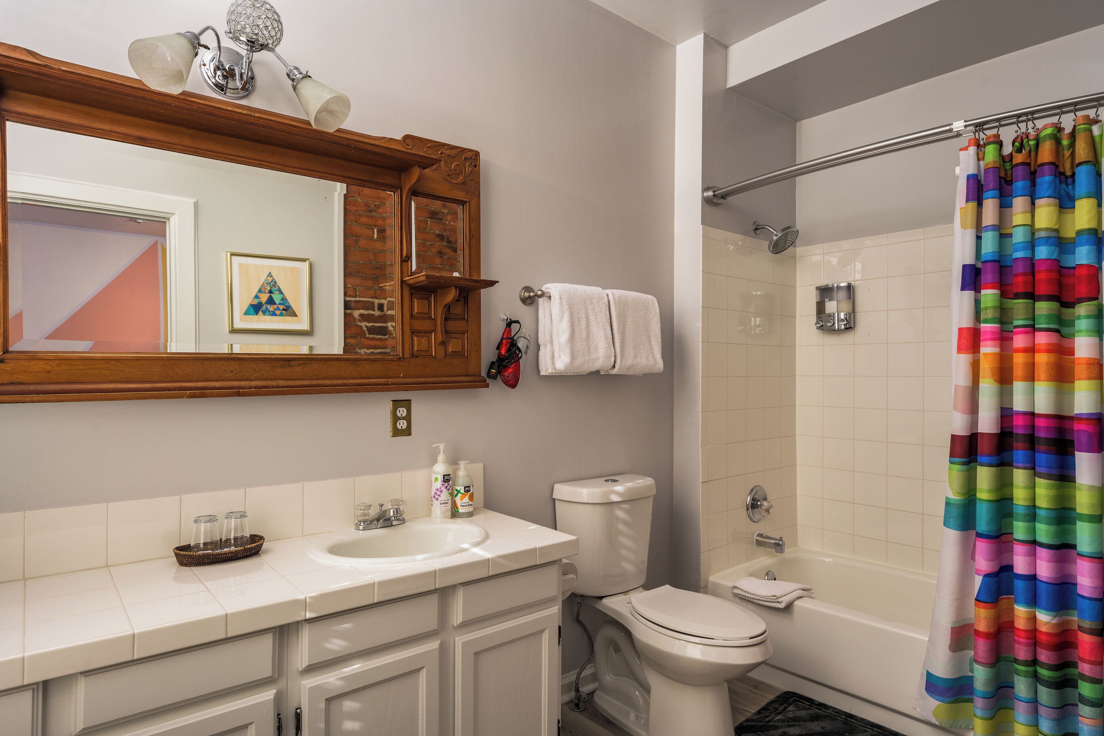 A bathroom with a white sink, toilet, and bathtub. There is a colorful shower curtain, a towel rack, and a framed picture on the wall.