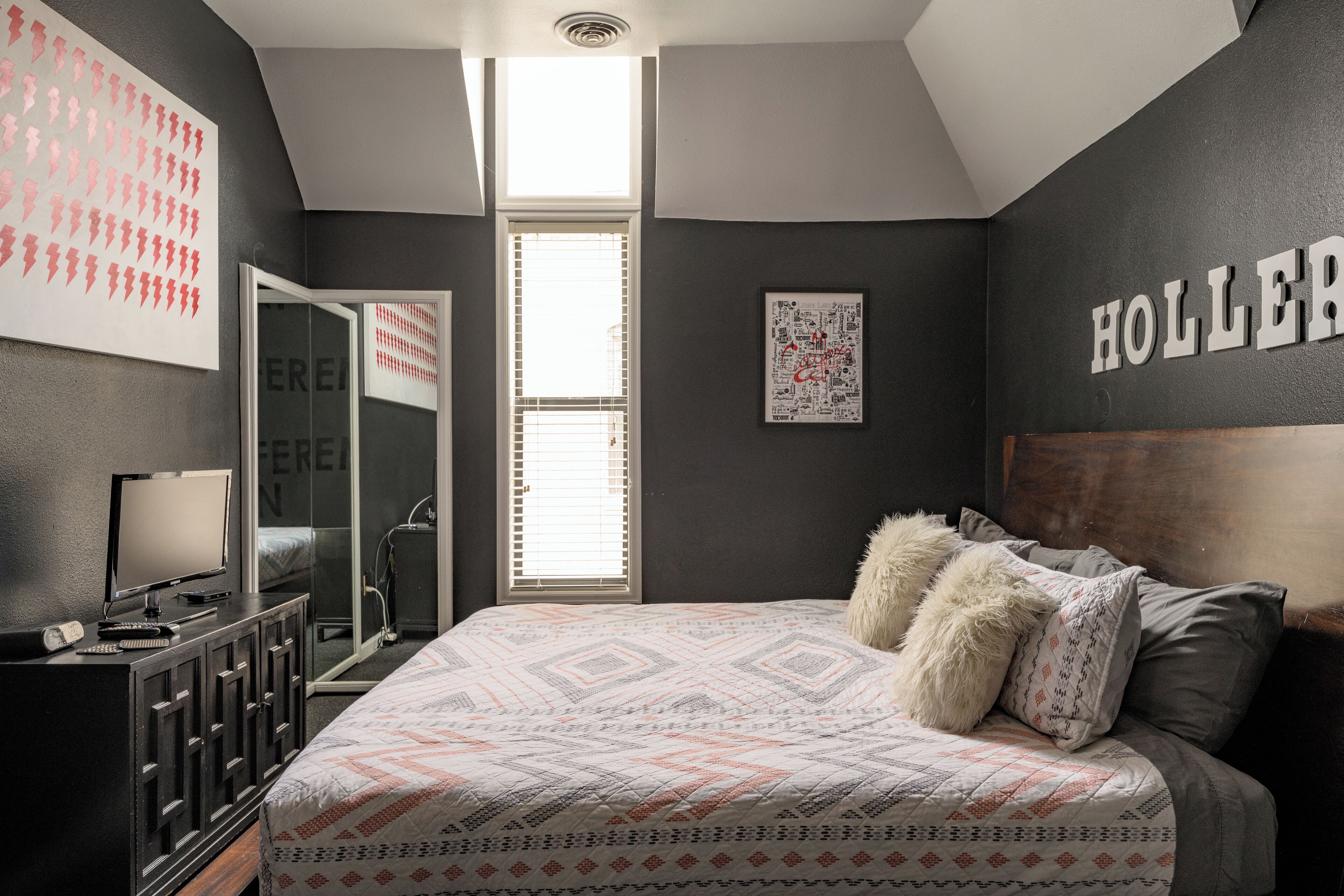 A bedroom with a bed, a dresser, a mirror, and a window.
