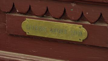 A brass plaque with the inscription "QUEEN ANNE INN" on a wooden surface with a decorative pattern.