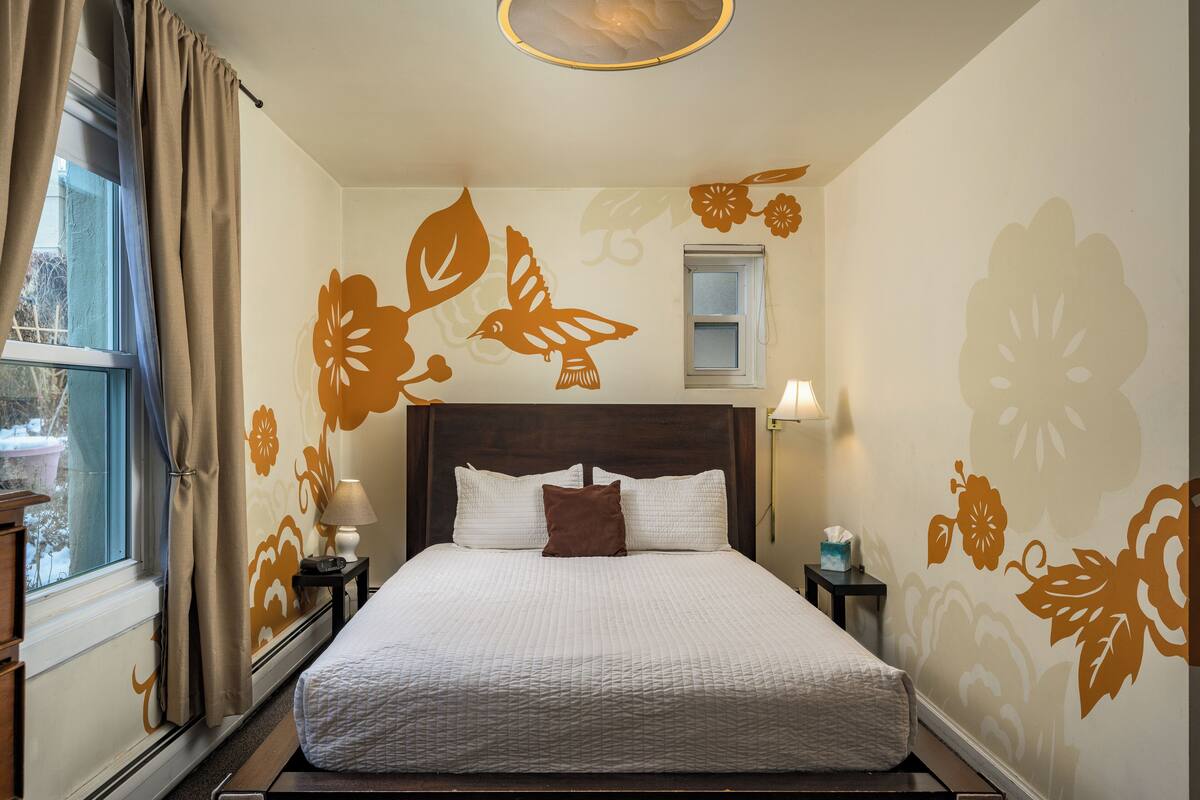 Un lit bien fait, avec un oreiller marron, une fenêtre avec des rideaux et des motifs floraux décoratifs sur les murs.