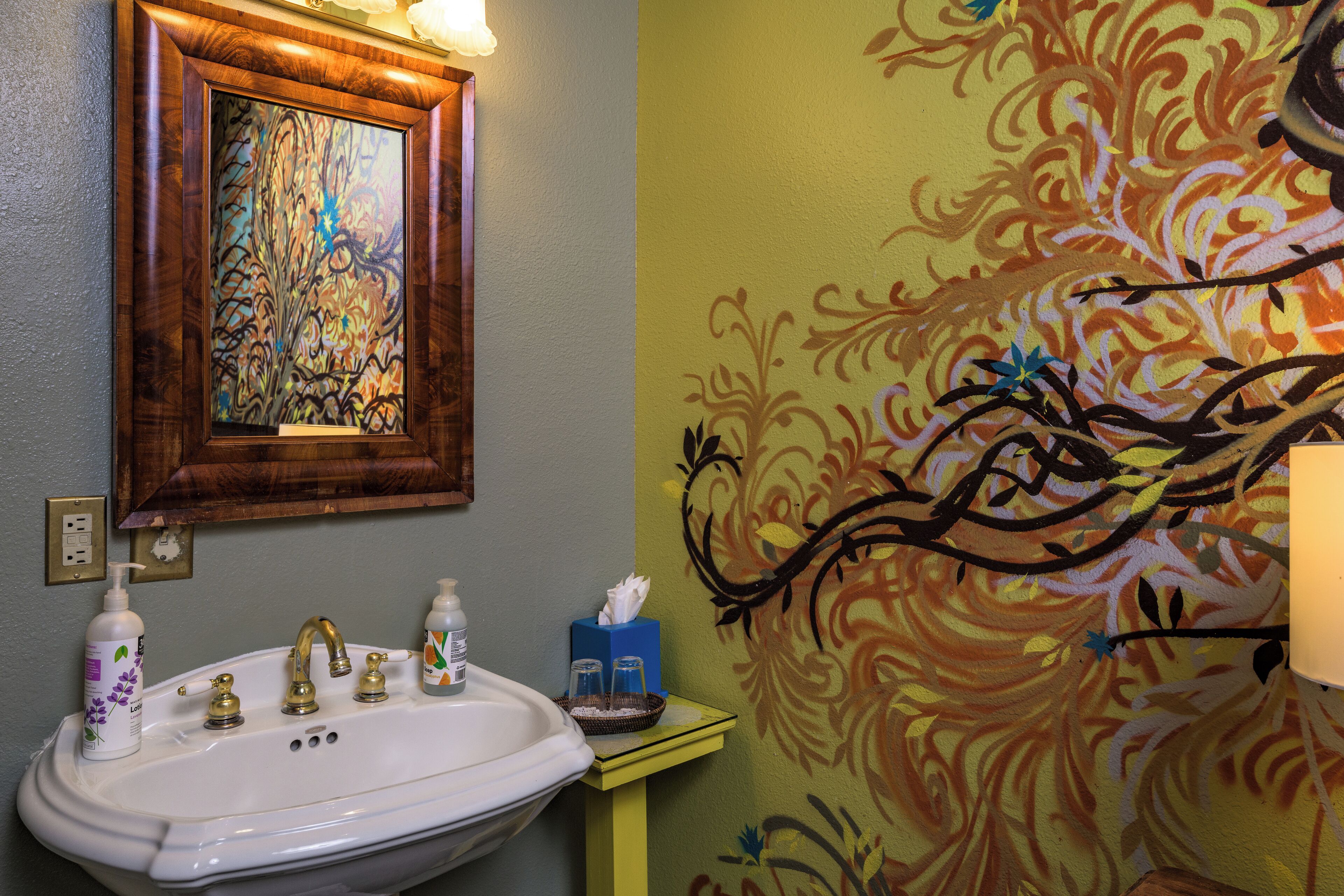 Casa de banho com lavatório branco, espelho e parede decorativa com motivos florais.