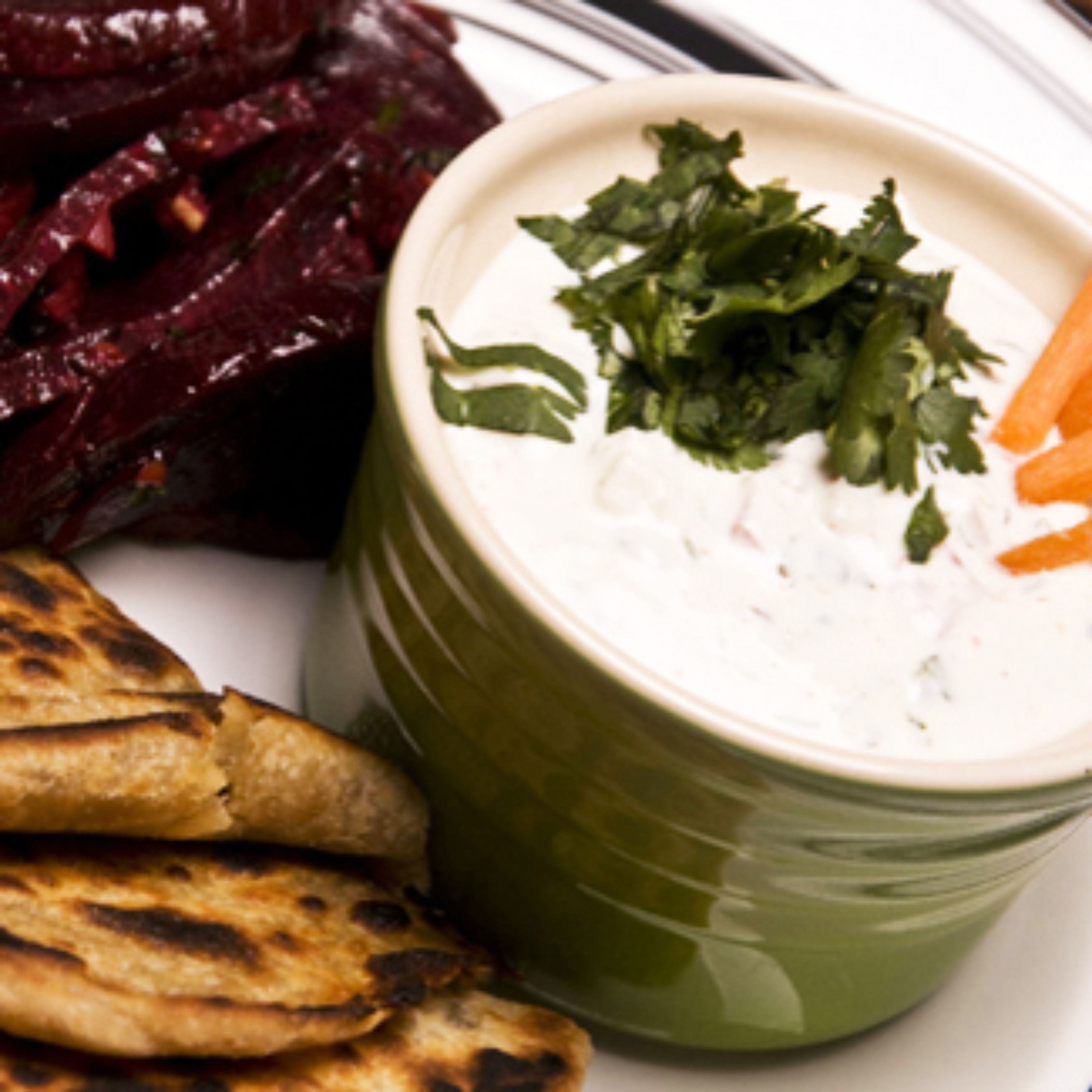 A plate with grilled flatbread, beetroot, and a bowl of white dip garnished with herbs.