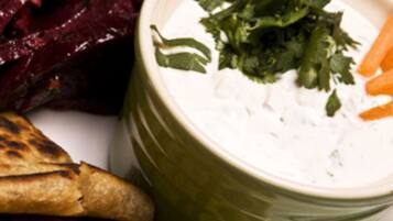 A plate with grilled flatbread, beetroot, and a bowl of white dip garnished with herbs.