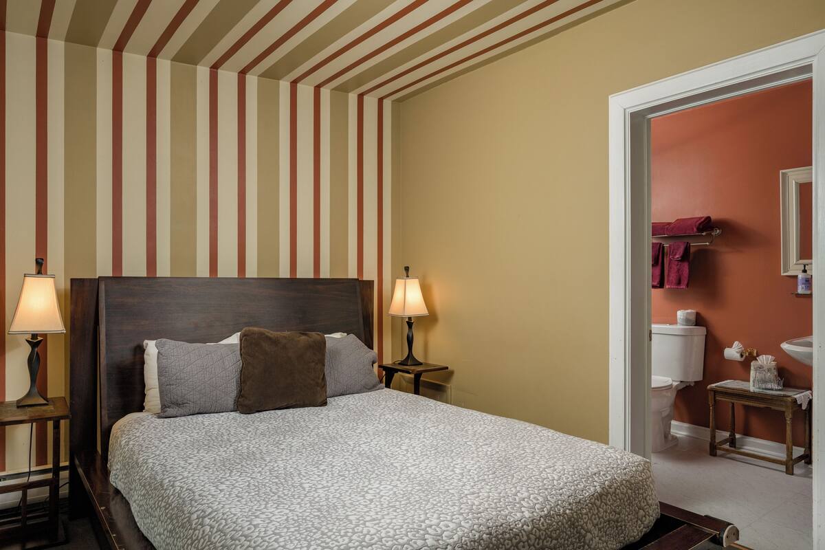 Une chambre d’hôtel avec un grand lit, deux lampes de chevet, une tête de lit en bois et un plafond à rayures.