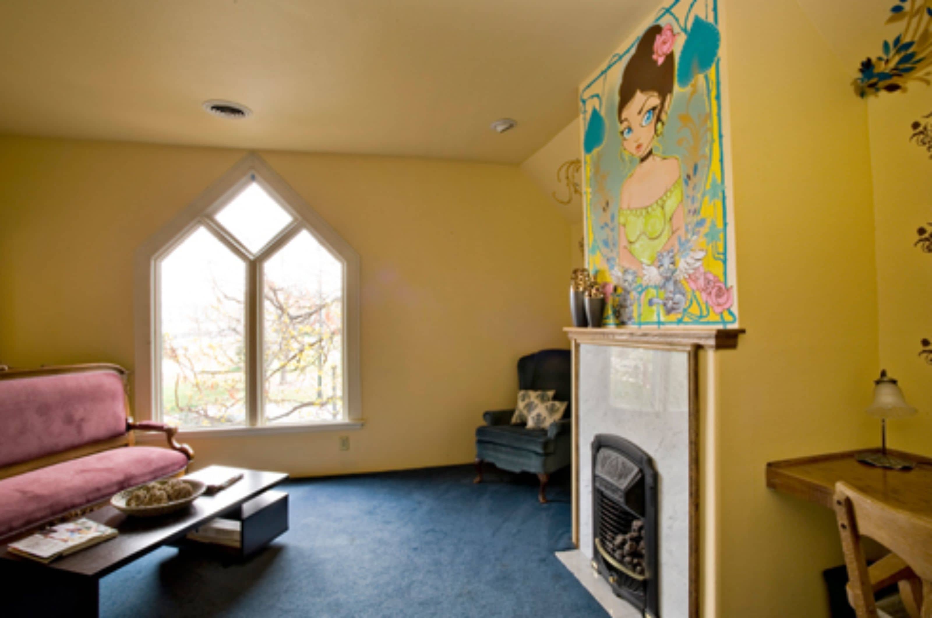 A living room with a pink sofa, a blue armchair, a fireplace, and a large window.