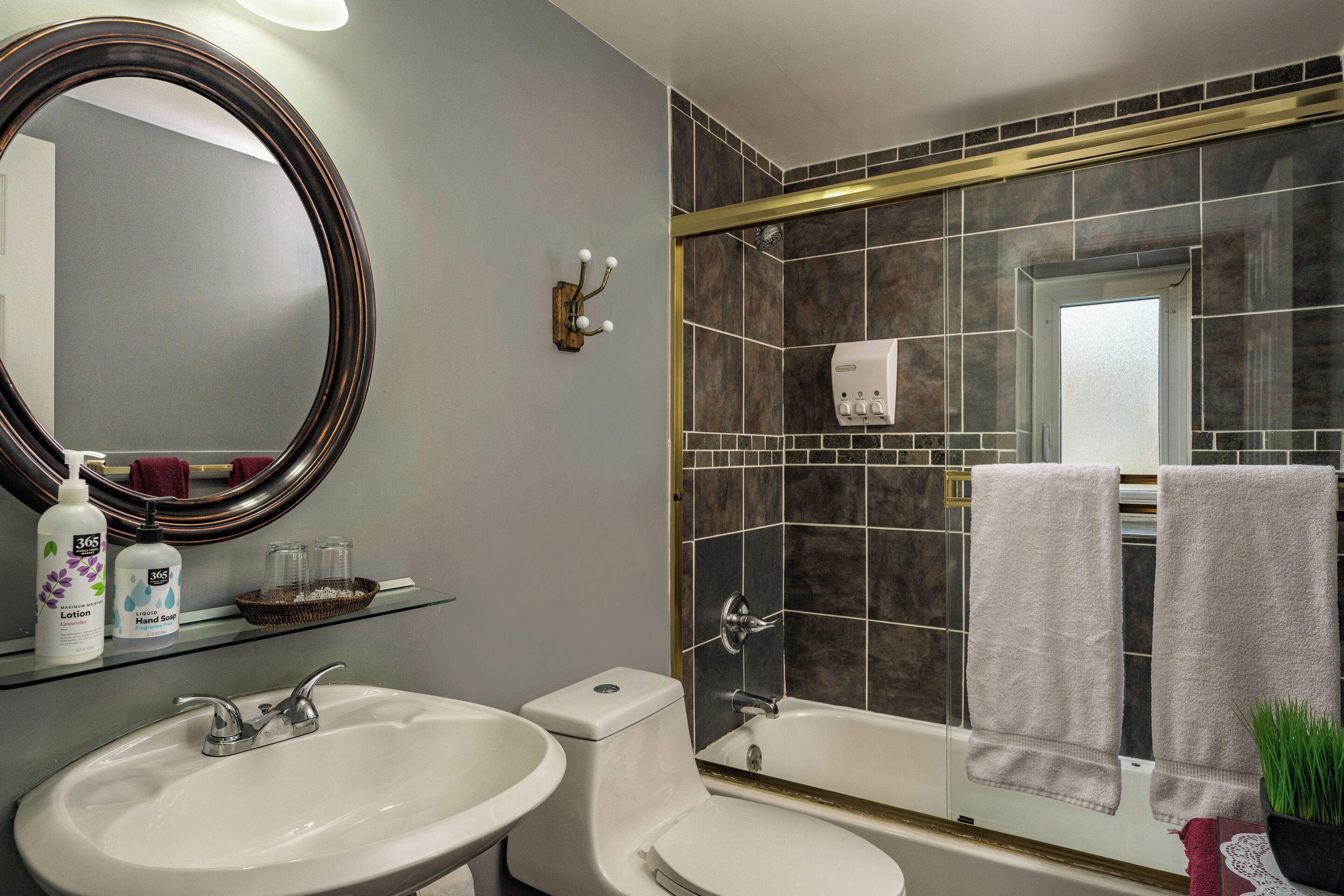 A bathroom with a white sink, a toilet, a bathtub, and a large mirror. There are towels hanging on the wall and a soap dispenser on the sink.