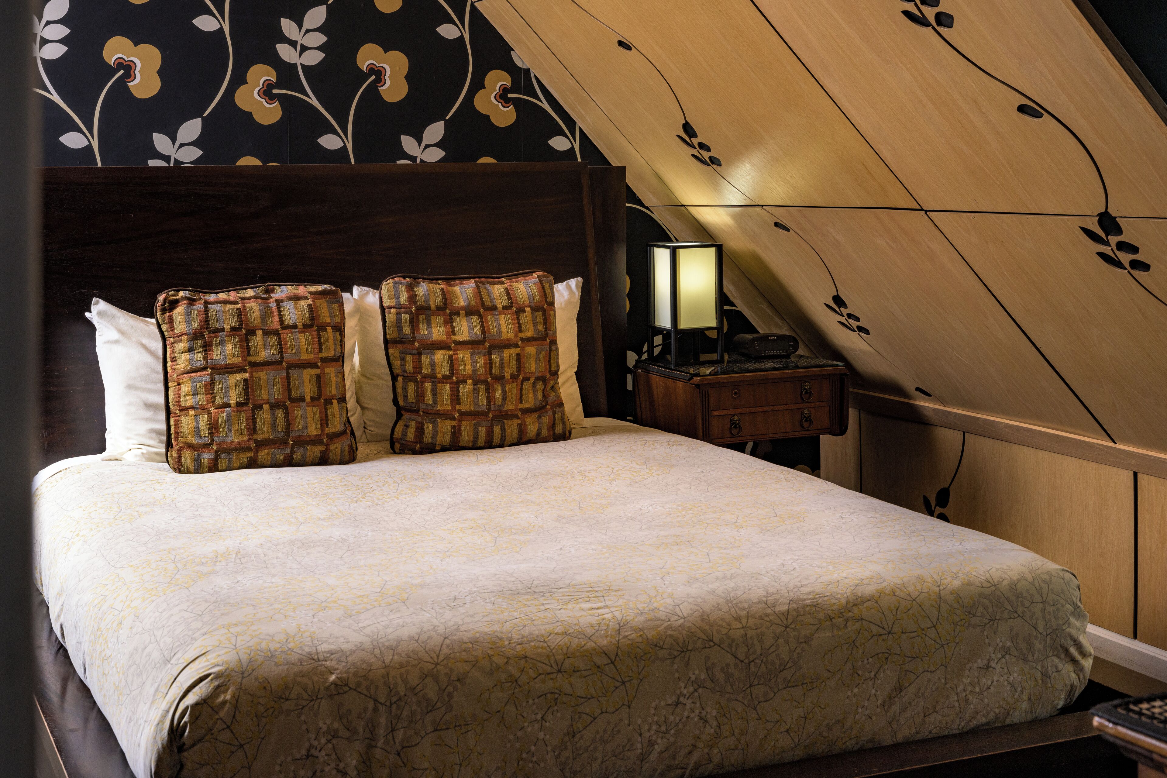 A neatly made bed with patterned pillows, a bedside lamp, and a wooden headboard.