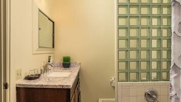 A bathroom with a marble sink, a small potted plant, a glass shower enclosure, and a towel rack.