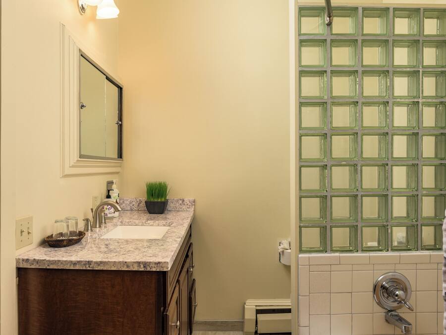 A bathroom with a marble sink, a small potted plant, a glass shower enclosure, and a towel rack.