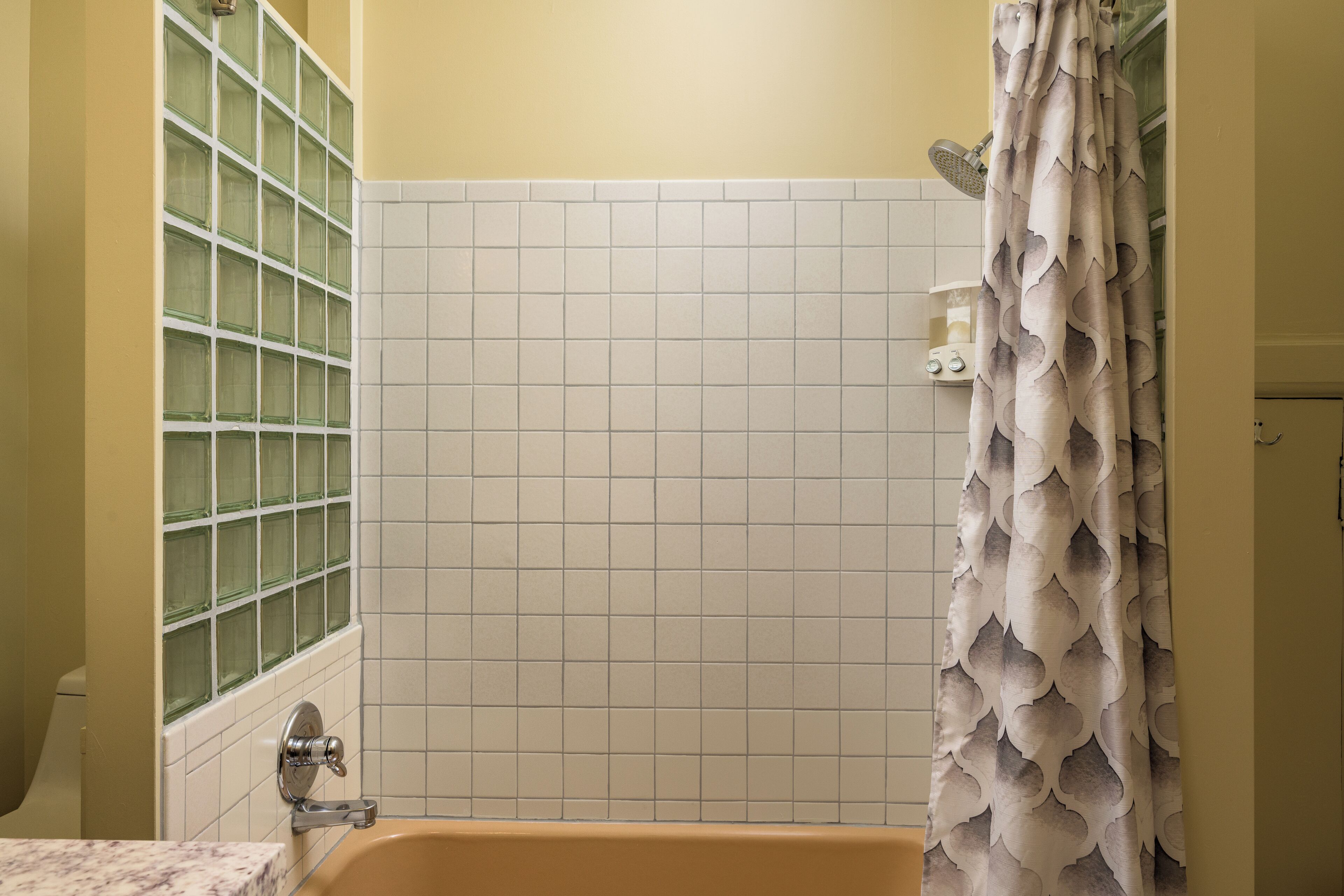 A bathroom with a bathtub, a shower curtain, and a tiled wall.