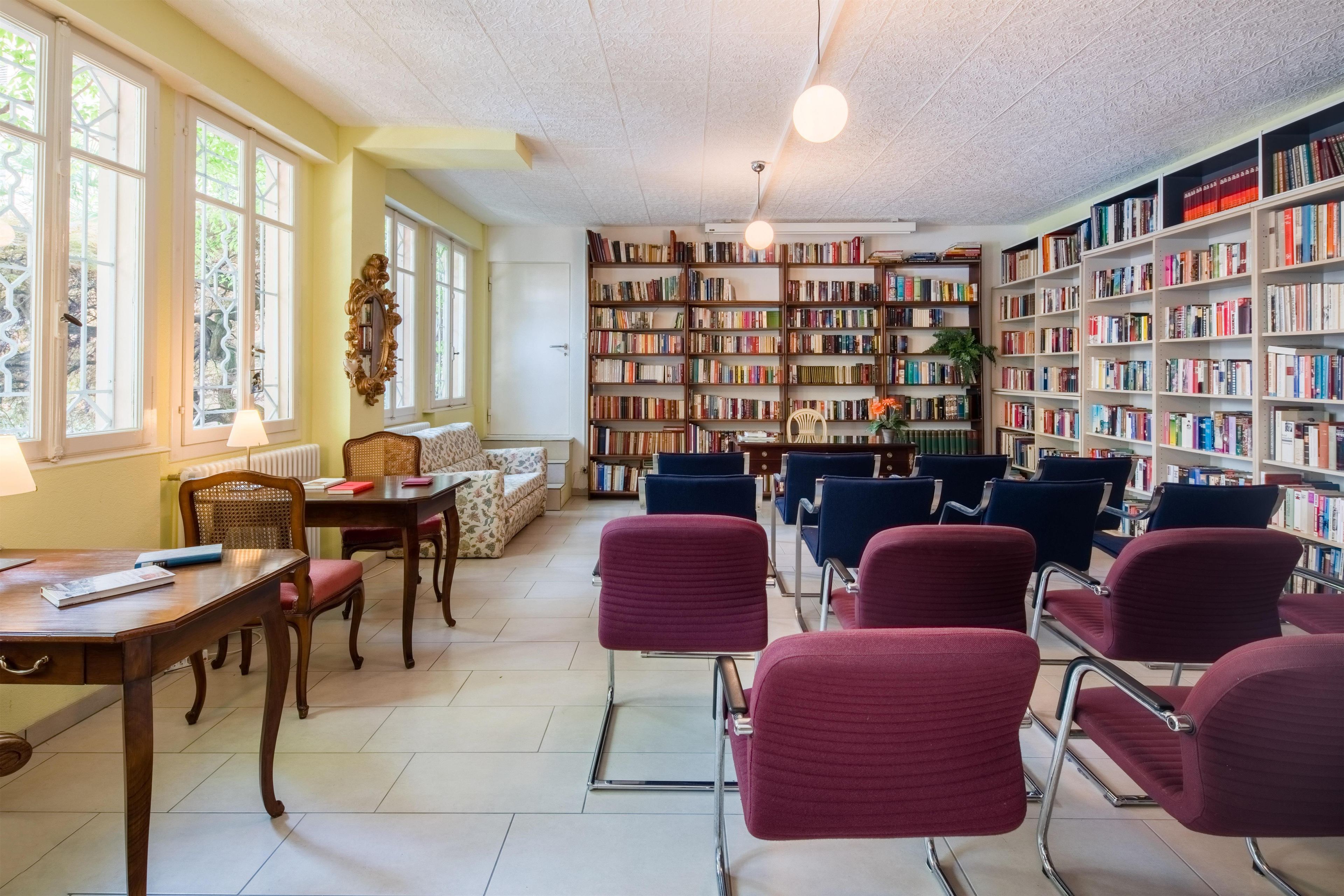Una biblioteca con estanterías, sillones de lectura, una mesa y un ventanal.