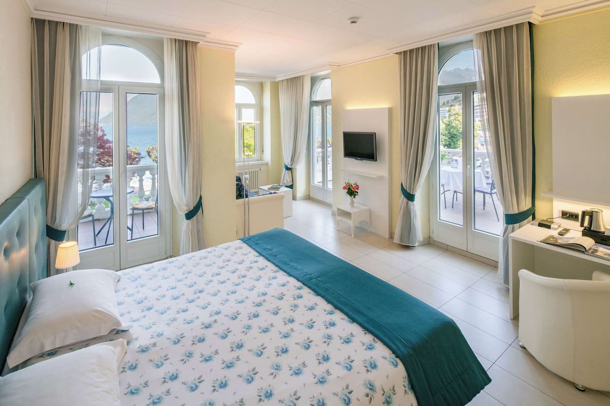 Habitación de hotel con una cama grande, un escritorio, un televisor y un balcón con vista al mar.