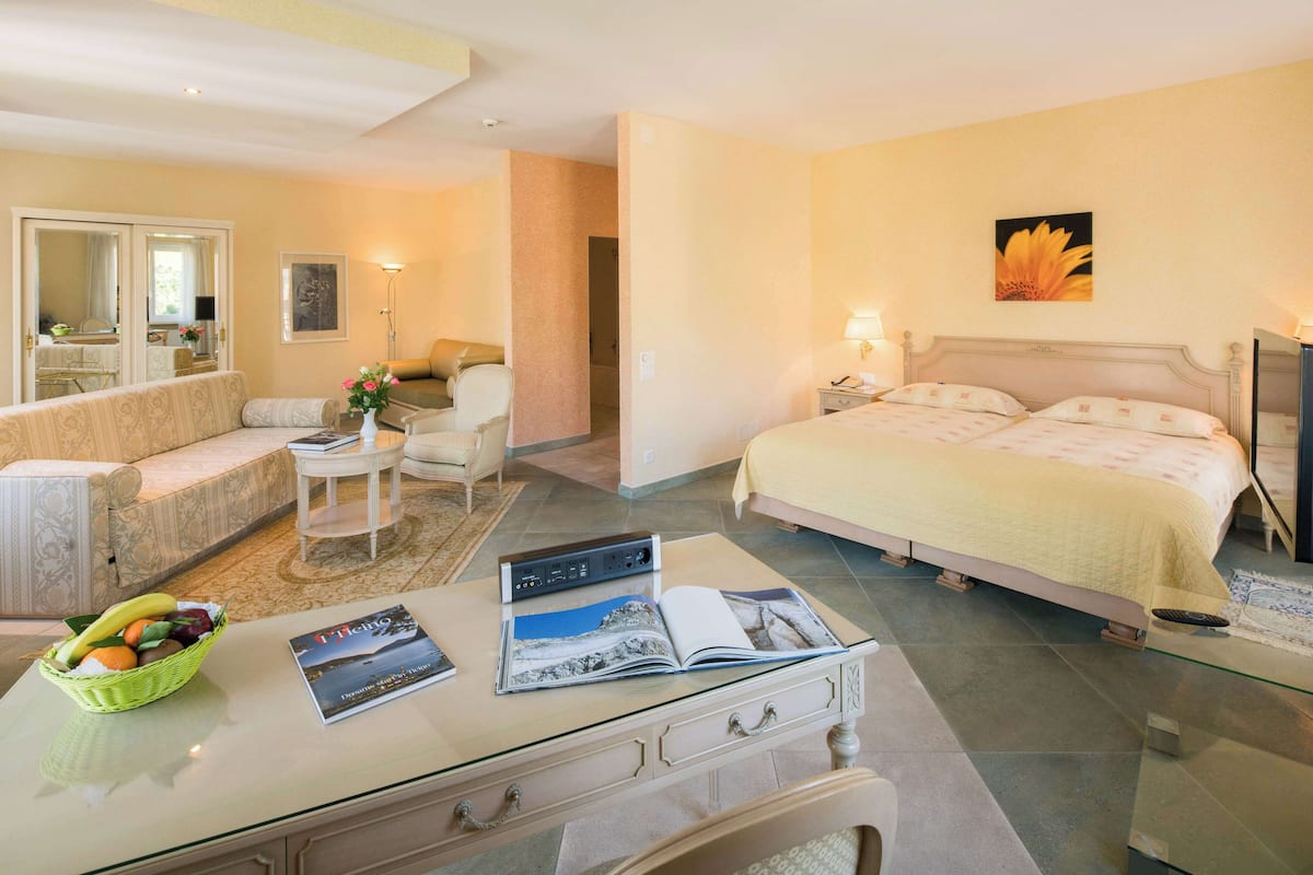 Habitación de hotel con cama, sofá, mesa de comedor y una cesta de fruta, además de una revista.