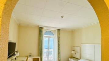 A hotel room with a bed, desk, TV, and a view through a glass door.
