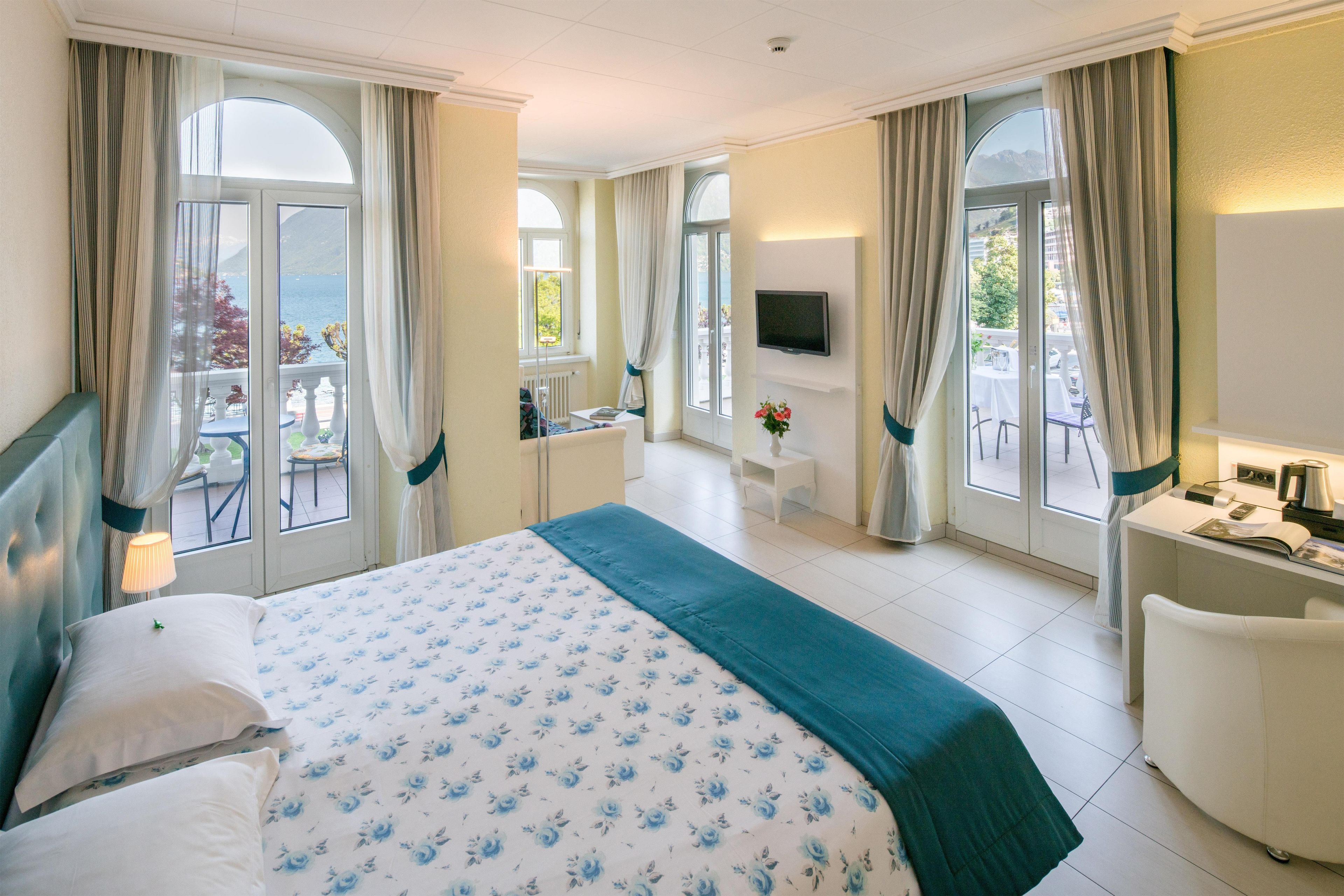 Une chambre d’hôtel avec un lit, un bureau, une télévision et de grandes fenêtres équipées de rideaux.