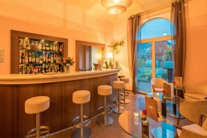 Un espace bar avec une table à plateau en verre, des tabourets de bar et une variété de bouteilles exposées sur des étagères.