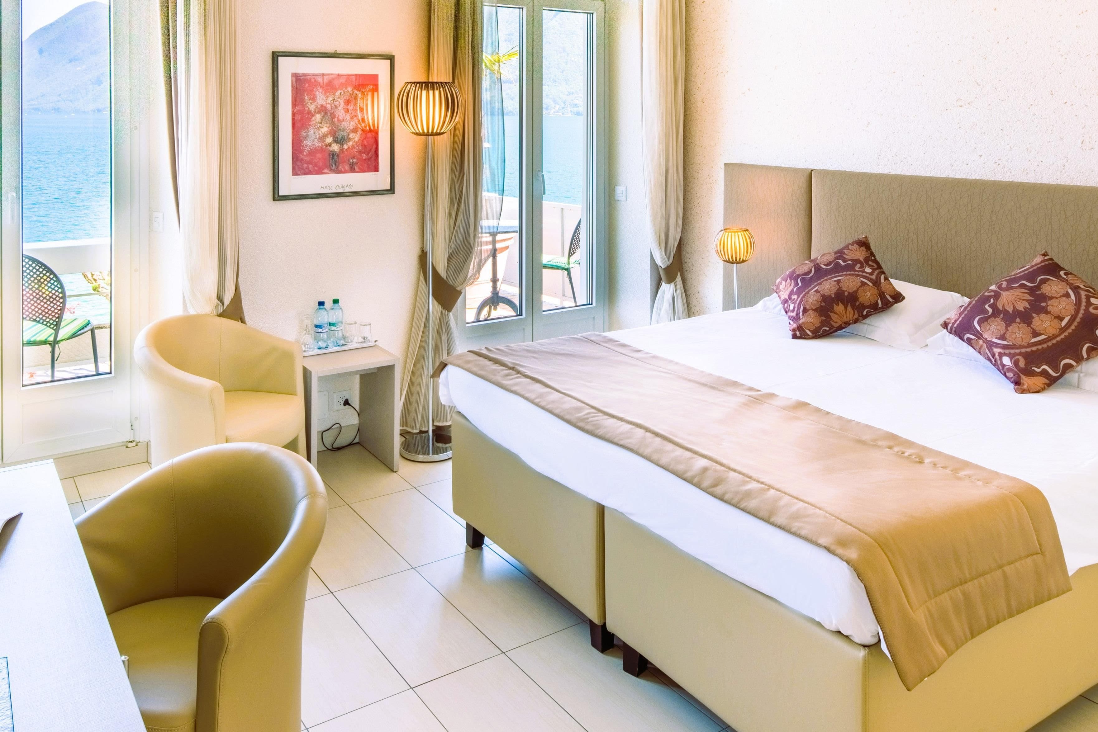 A hotel room with a bed, a chair, a small table, and a window with a view of the sea.