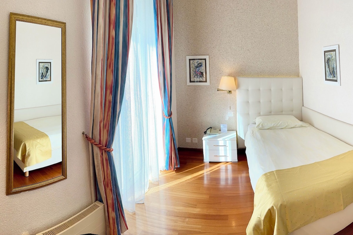 Una habitación de hotel con cama, mesita de noche, lámpara y espejo.