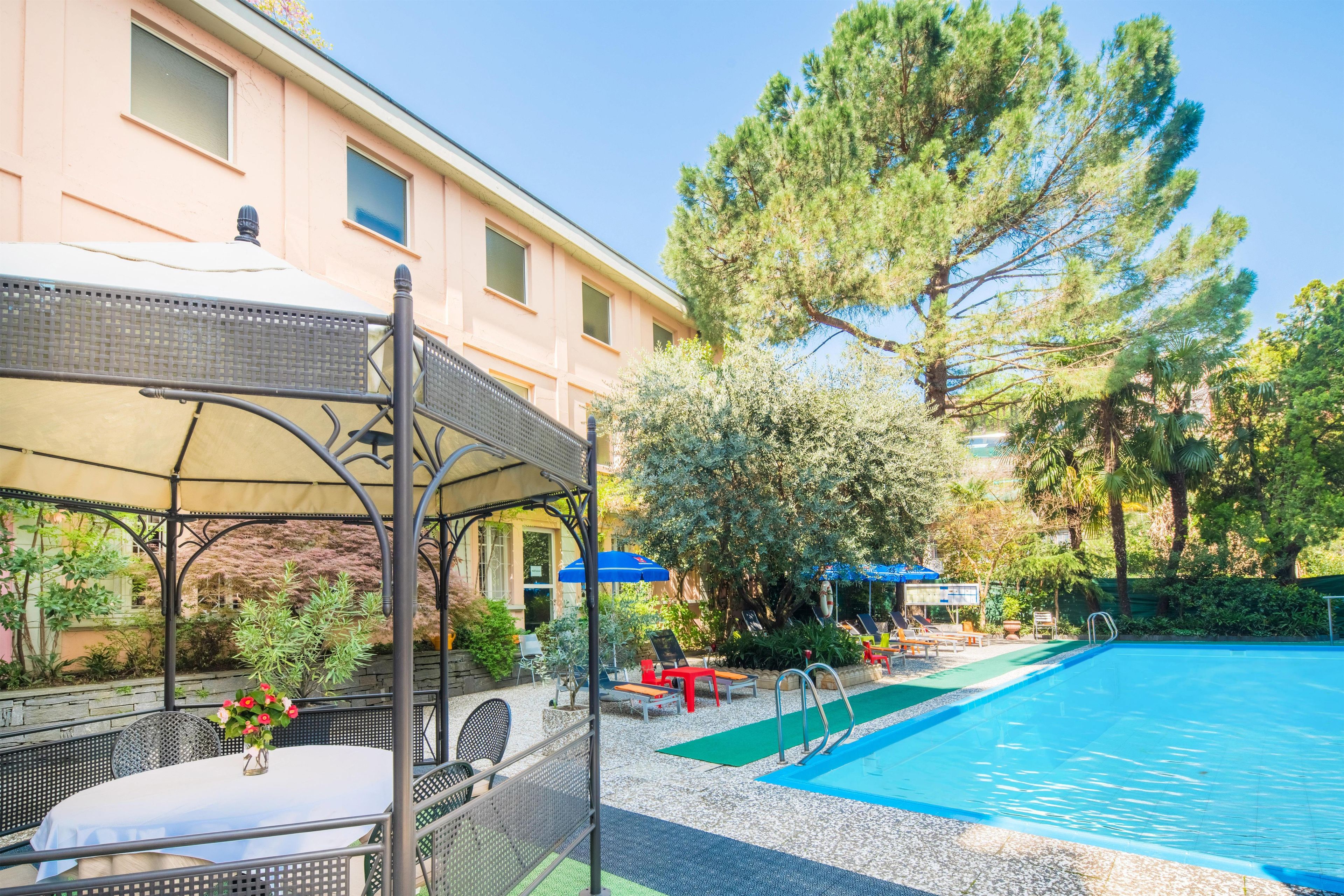 A pool area with a covered seating area and a building in the background.