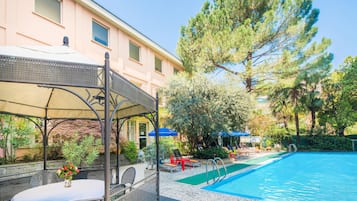 A pool area with a covered seating area and a building in the background.