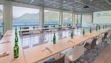 A conference room with a long table, chairs, and a projector screen displaying 'Best Western Hotel Bellevue au Lac Lugano, Switzerland Conference Centre'.