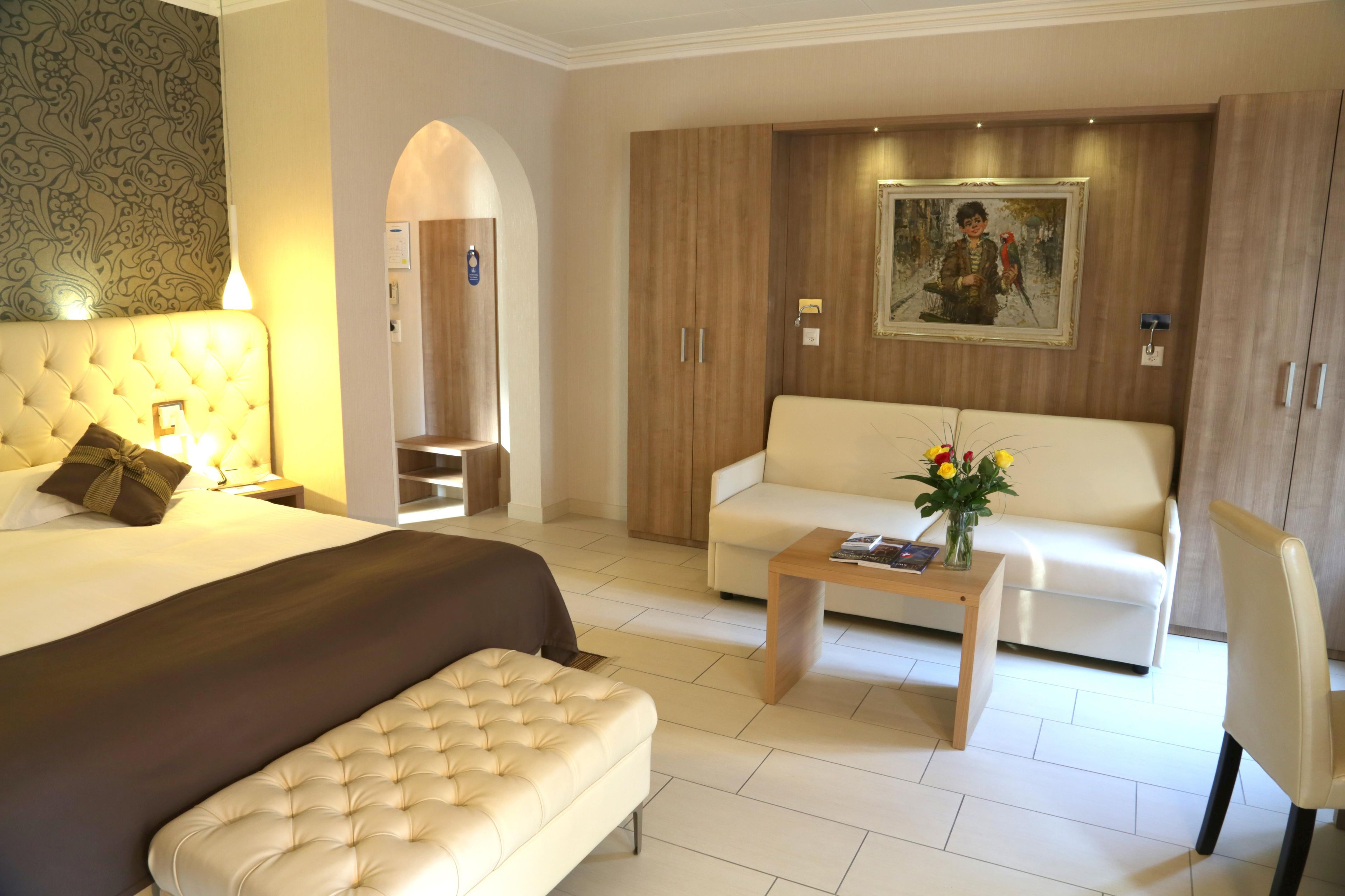 A hotel room with a bed, a sofa, a coffee table, and a chair.