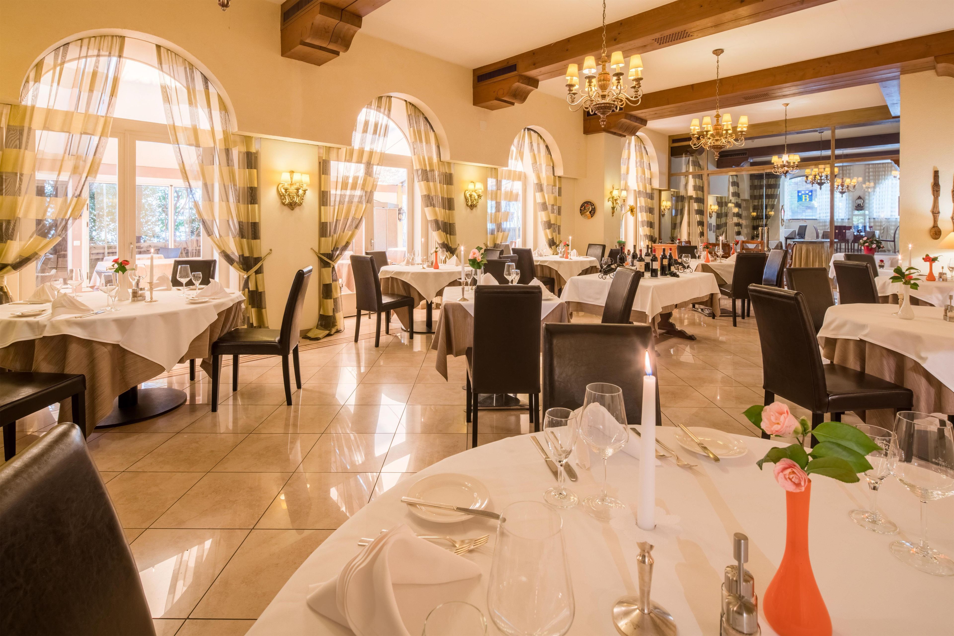 Un restaurant doté de plusieurs tables rondes, chacune recouverte d’une nappe blanche et agrémentée de bougies et de verres à vin.